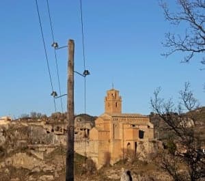 Un poste de luz de madera y al fondo la colegiata de Naval. H. J.