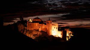 Colegiata de Alquézar iluminada al anochecer, con un cielo de nubes rojizas.