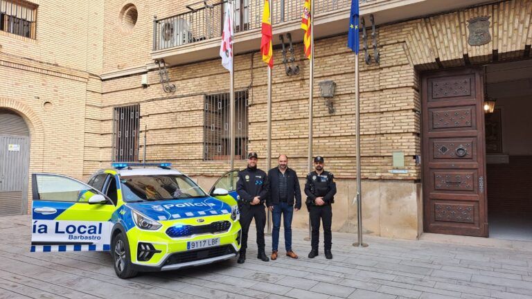 Nuevo coche de la Policía Local de Barbastro con rotulación azul y amarilla junto a tres personas ante el Ayuntamiento.